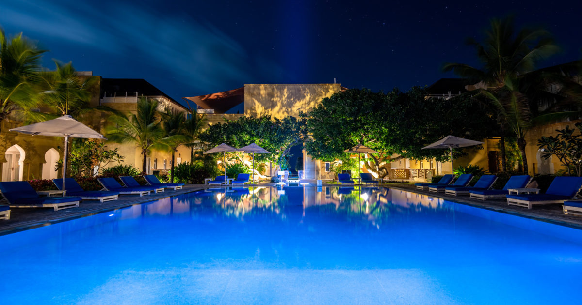 An illuminated resort pool surrounded by palms at dusk